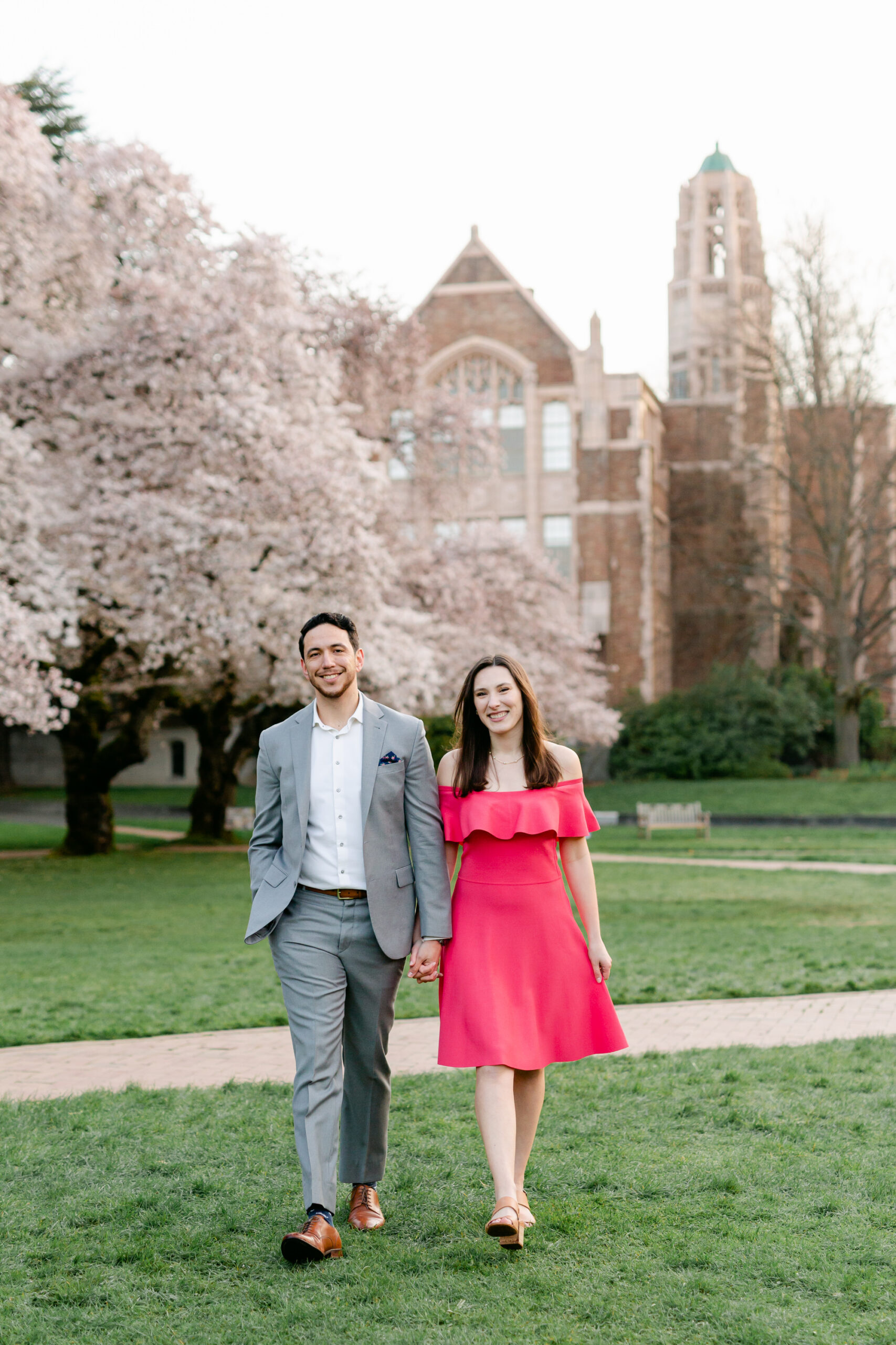 A couple walks together in front of cherry blossoms at UW in Seattle.