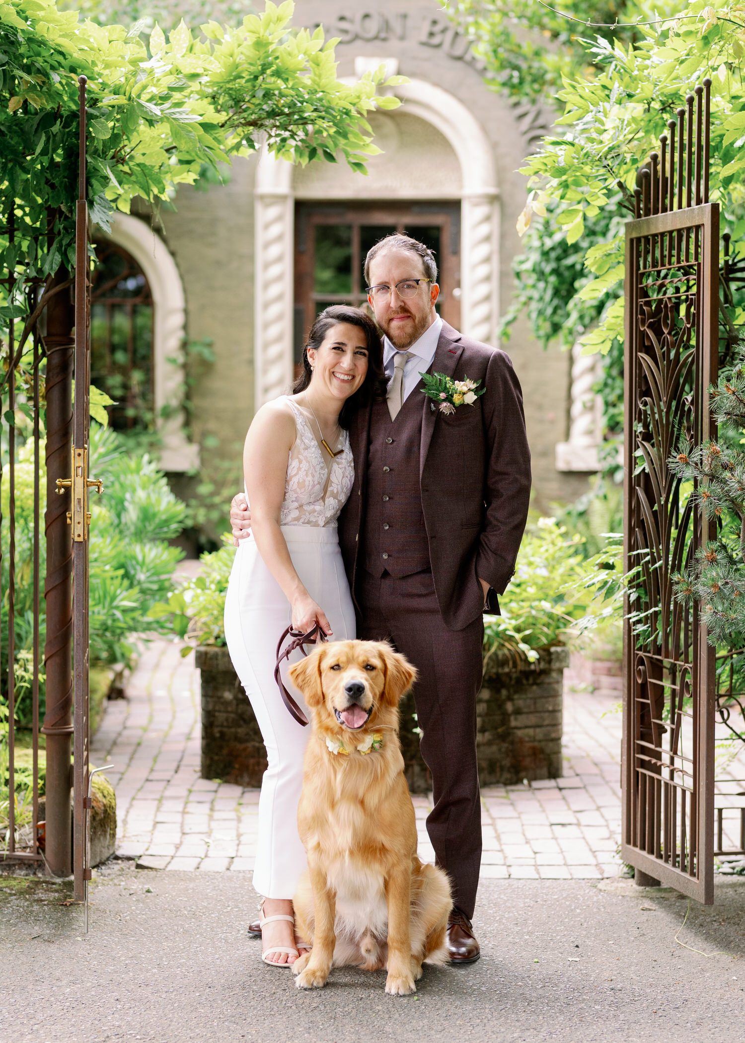 Bride, groom, and their golden retriever posing in front of The Corson Building