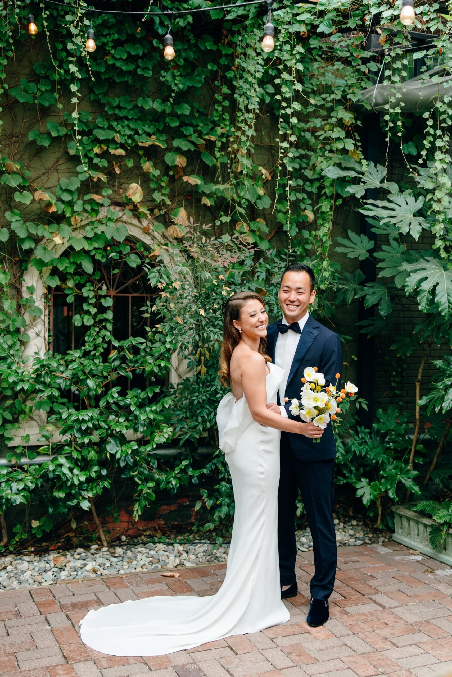 A couple smiles and stands in front of a vine-covered wall at the Corson Building.