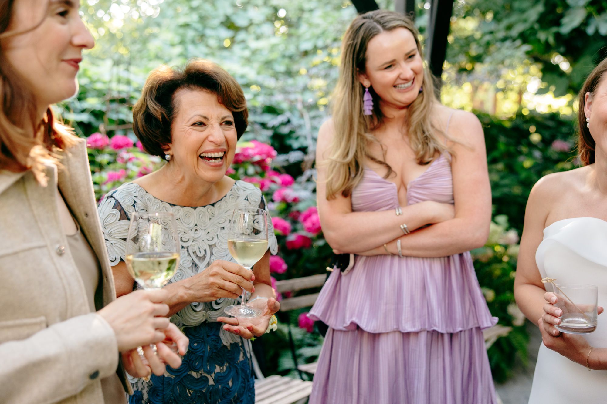 Wedding guests laugh and chat during cocktail hour outside.