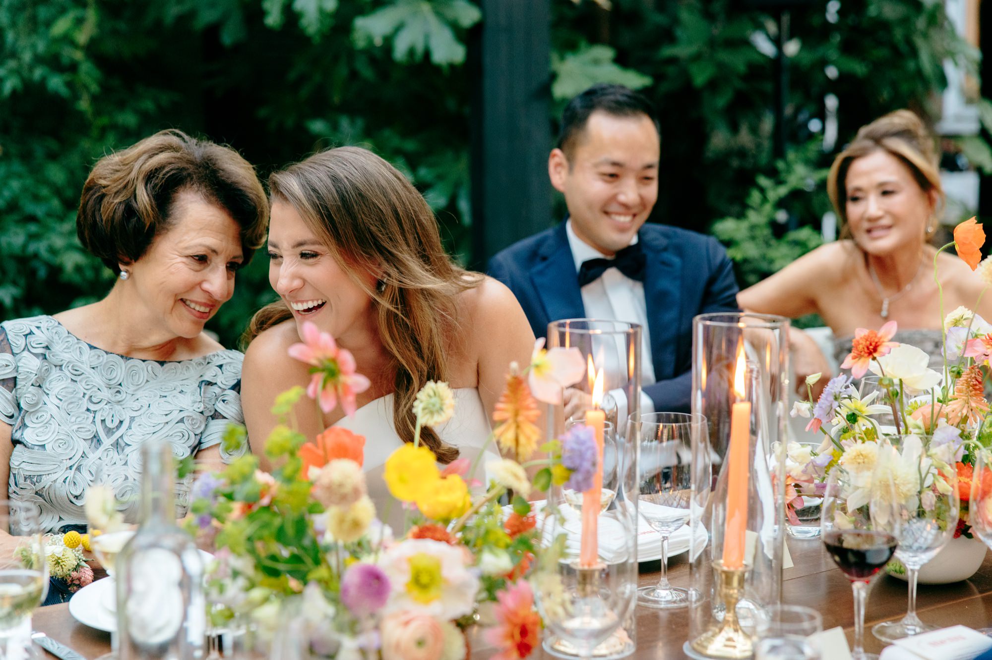The couple laughs with their weddings guests at a candlelit dinner outside.