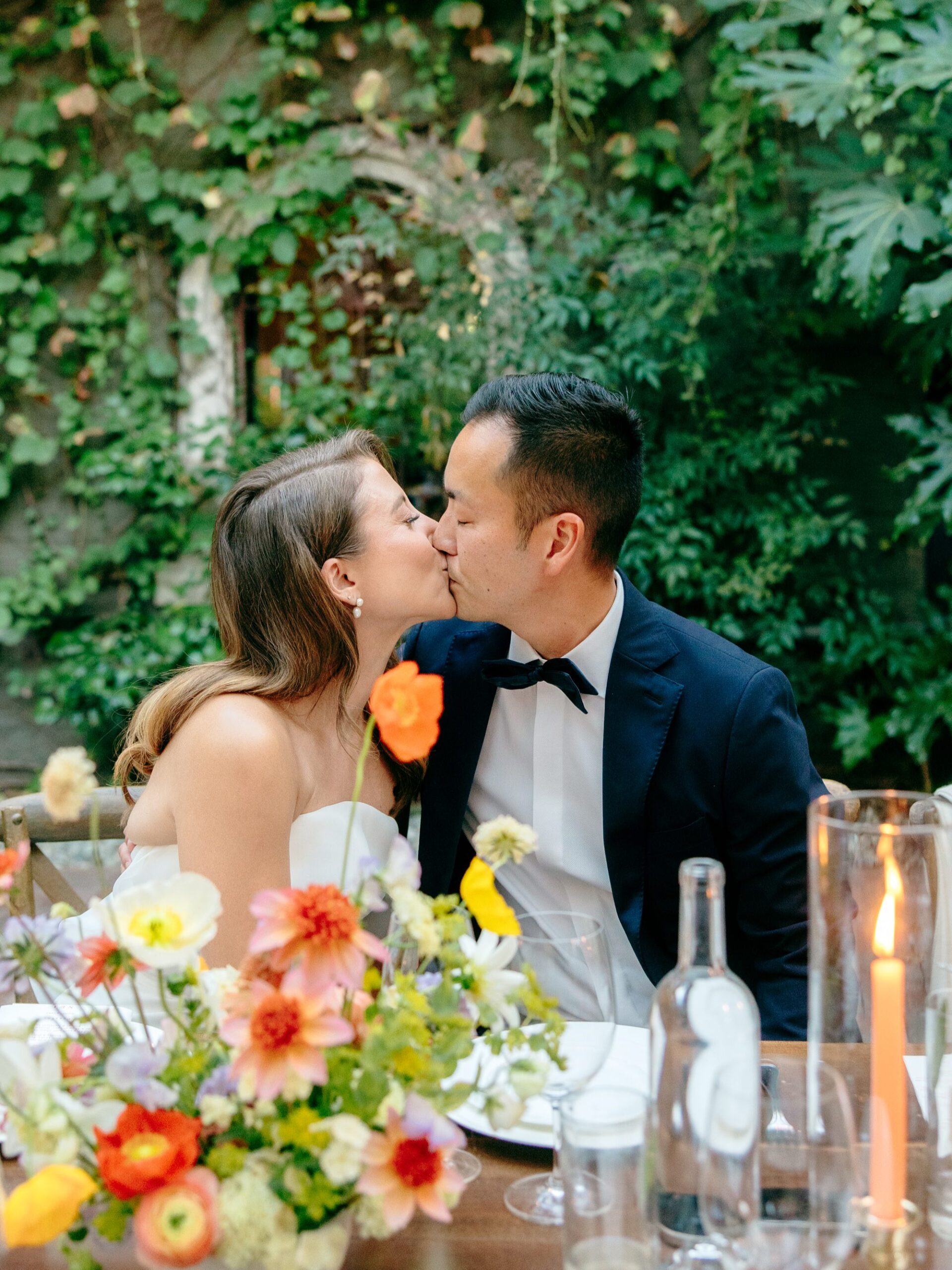 A couple kisses in the courtyard at the Corson Building with the vine-covered building in the background.
