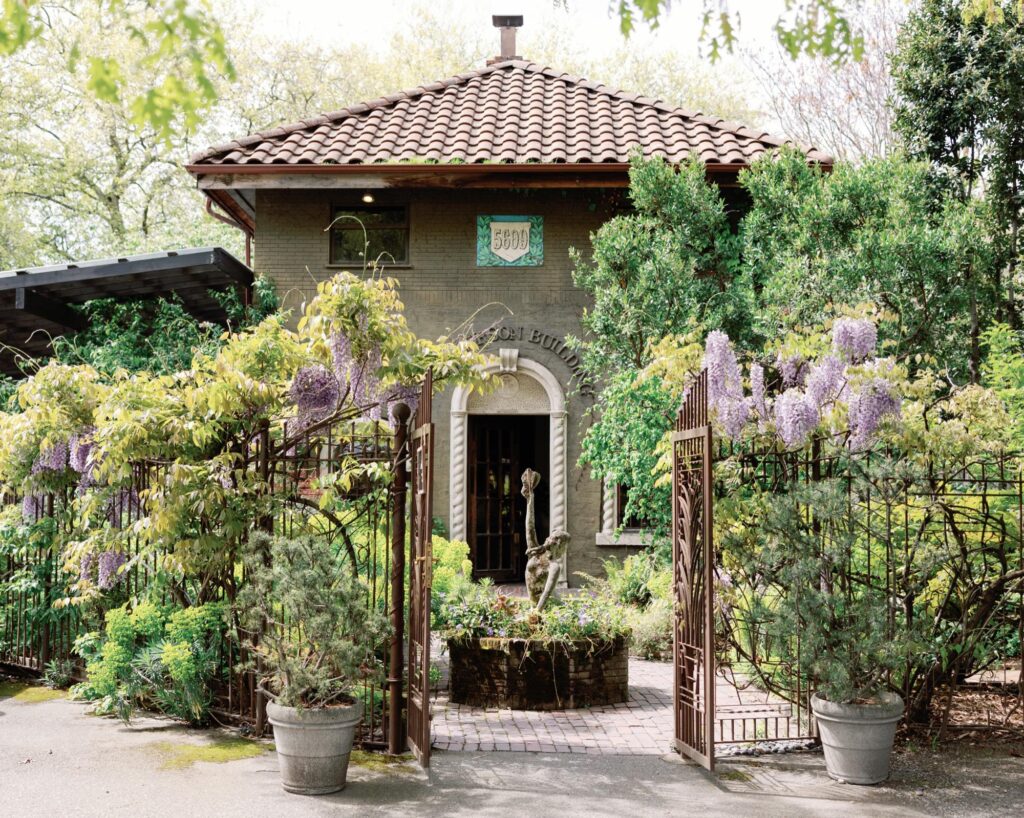 The exterior of the Corson Building with a charming garden, featuring blooming wisteria and a rustic entrance gate.