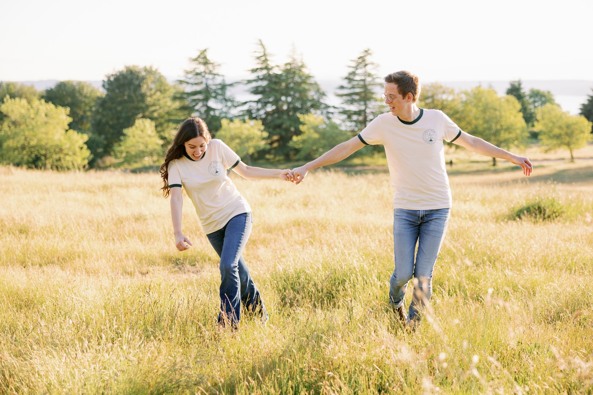 A couple in matching shirts playing and laughing in a grassy field at Discovery Park.
