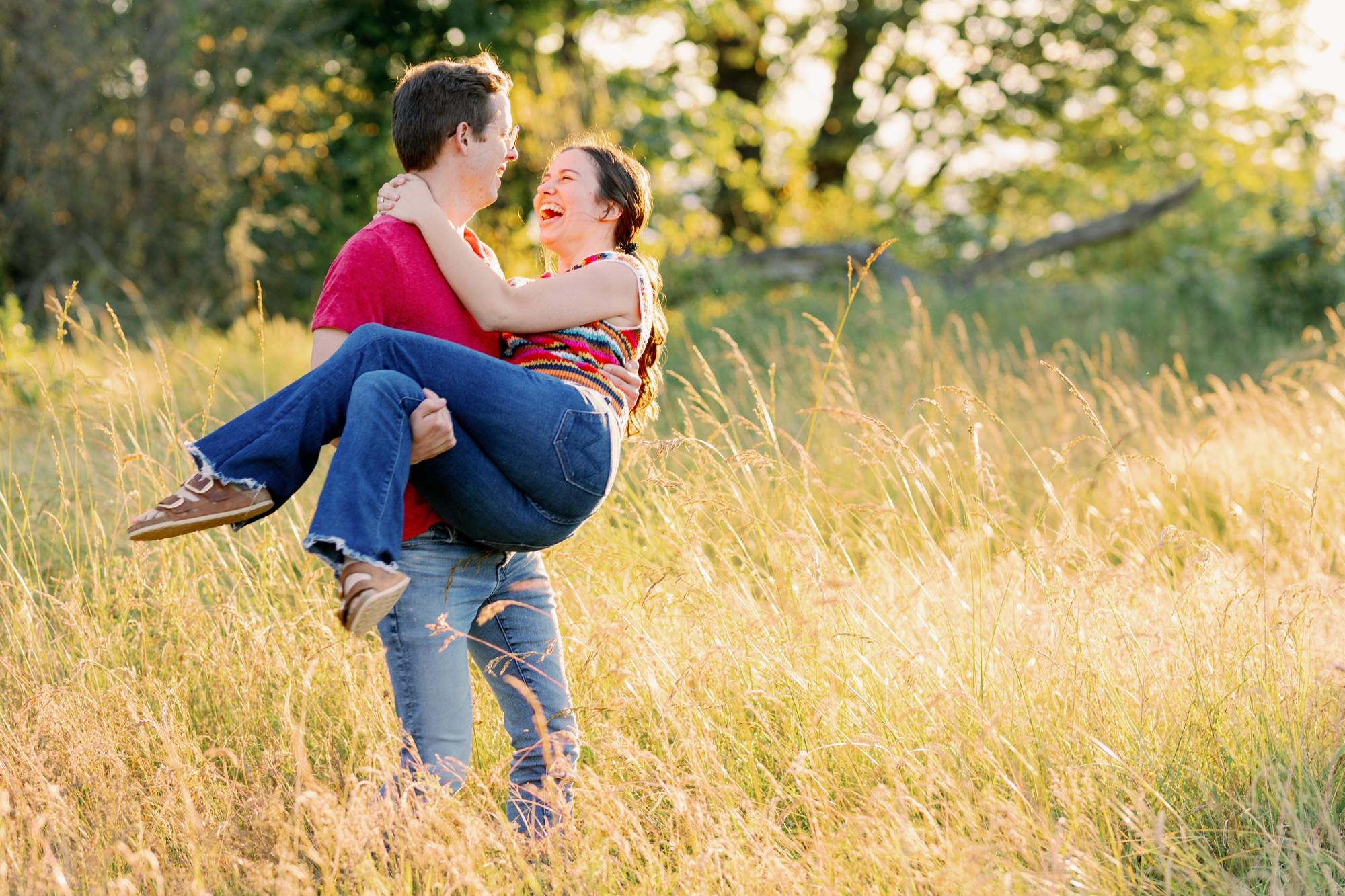 A man lifting his partner in his arms as they share a kiss, both smiling brightly in a sunny field.