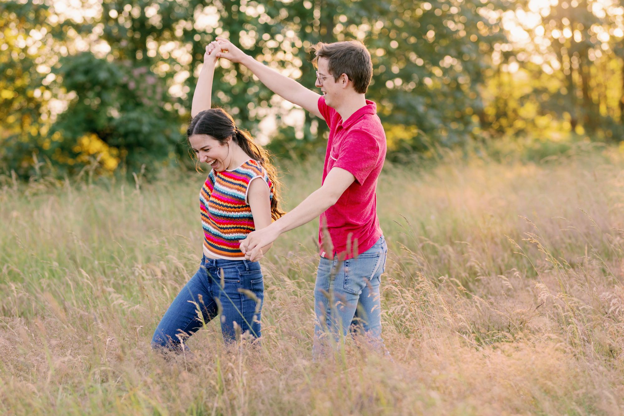 A couple holding hands and spinning in a grassy field, smiling and enjoying their time together.