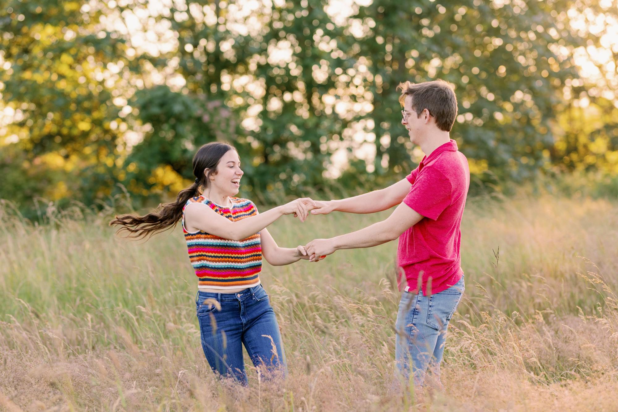 A couple dancing in a grassy field, with the woman wearing a colorful knit vest and the man in a red shirt.