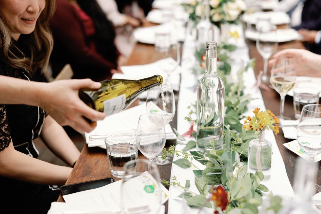 Close-up of an elegantly set wedding table with greenery, flowers, and glasses being filled with wine.