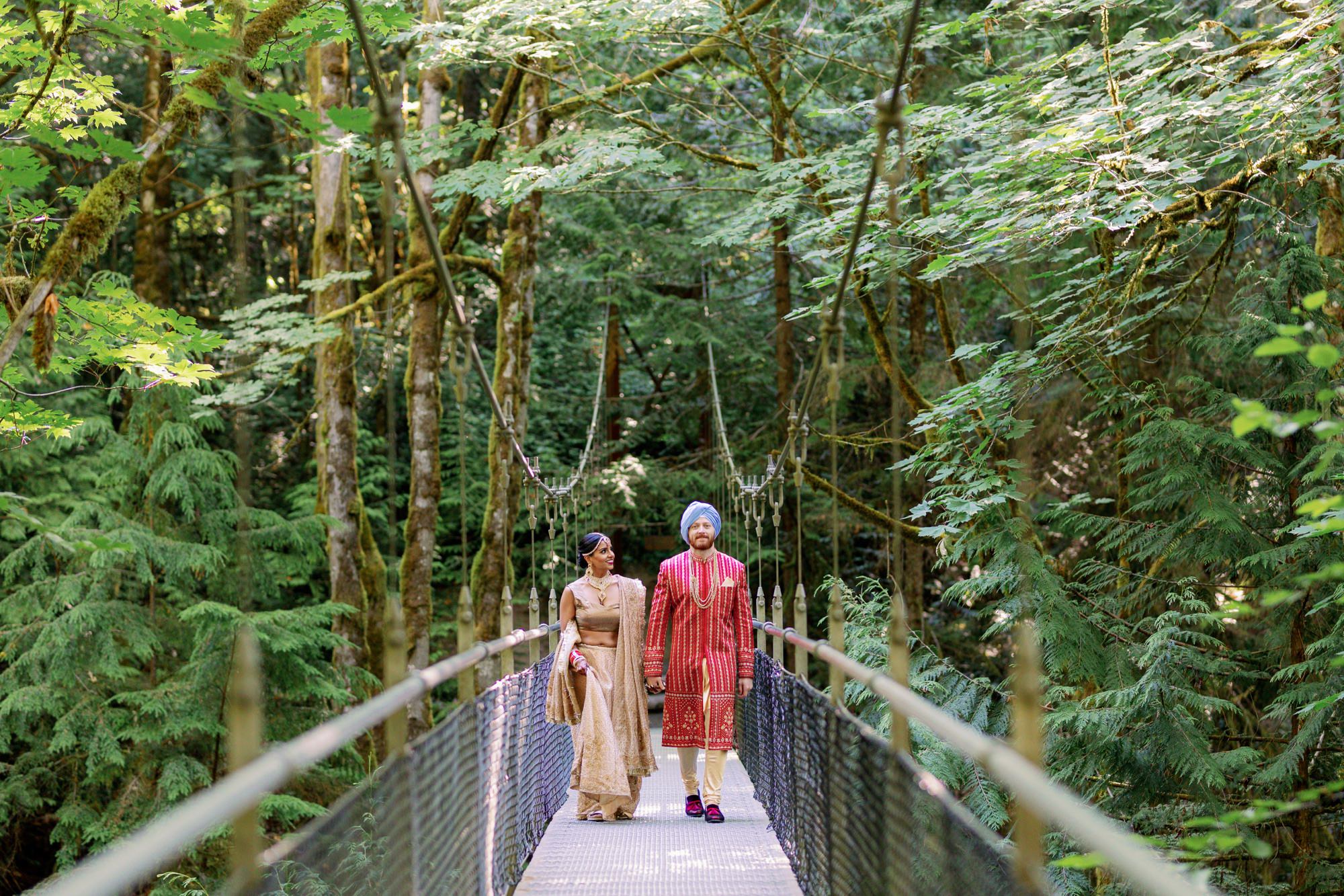 Bride and groom standing together on a forest bridge, holding hands and smiling.