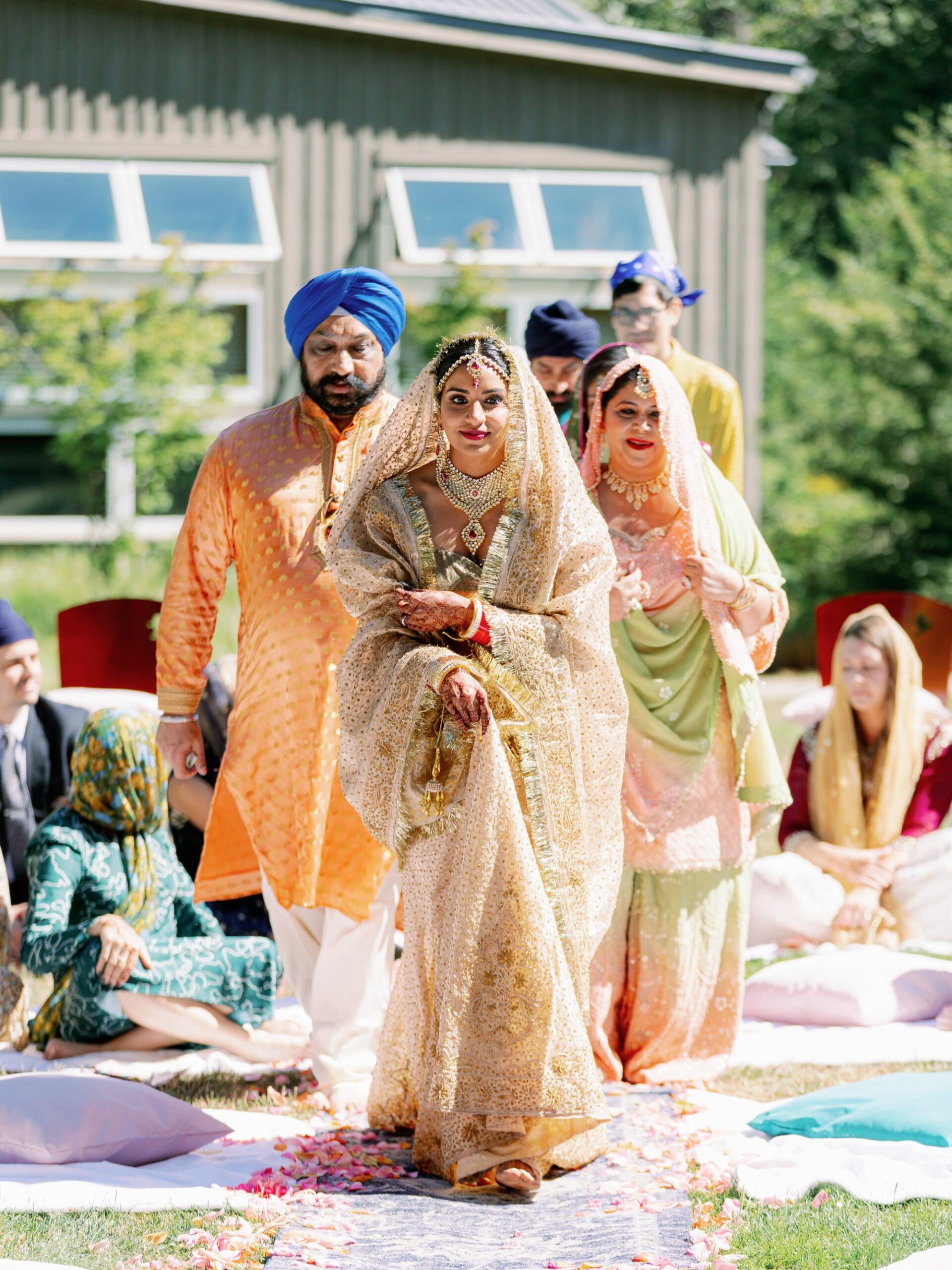 The bride, escorted by her family, walks towards the ceremony area, surrounded by guests.