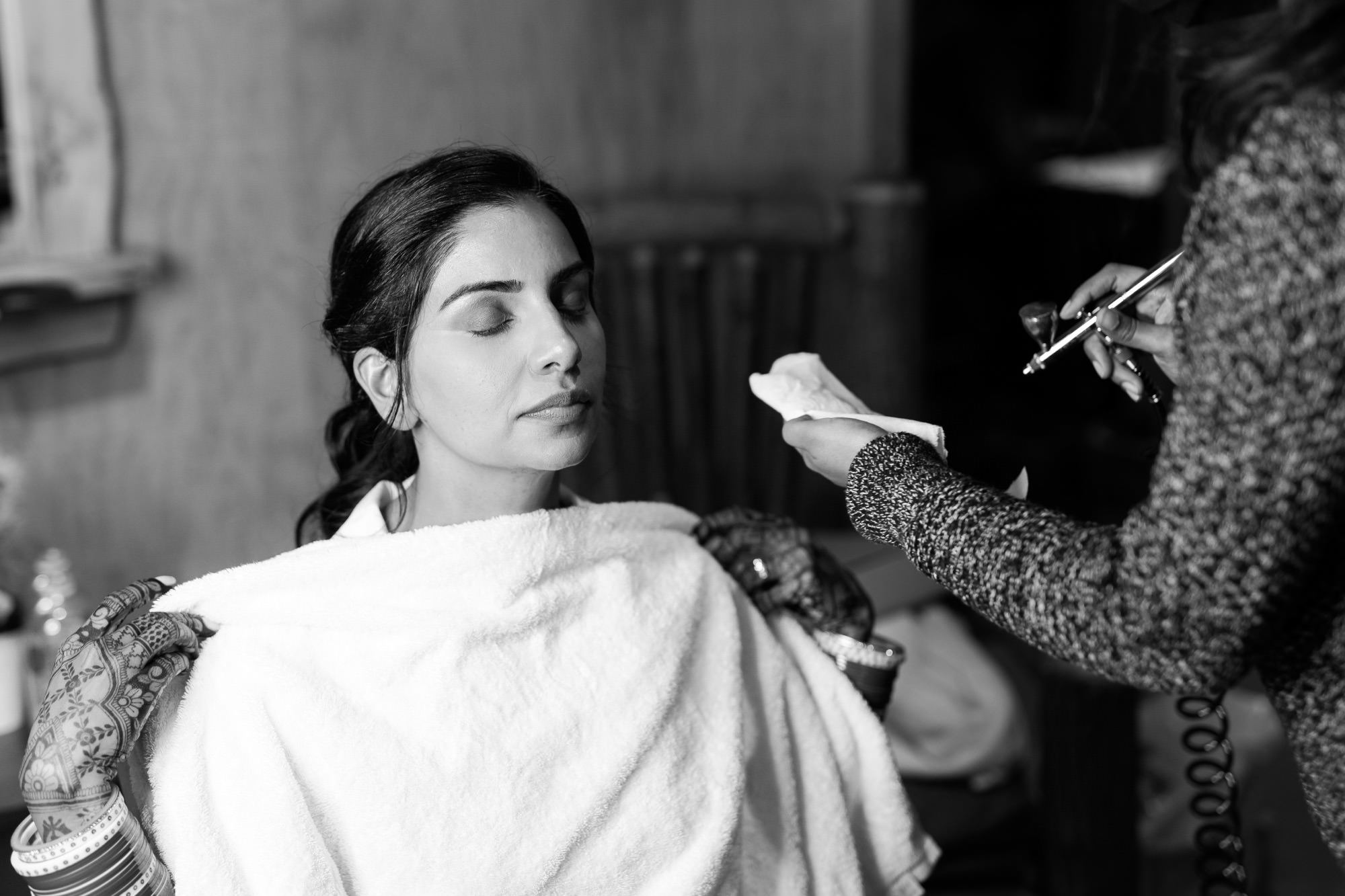 Bride with closed eyes receiving a final makeup touch-up before the wedding ceremony.