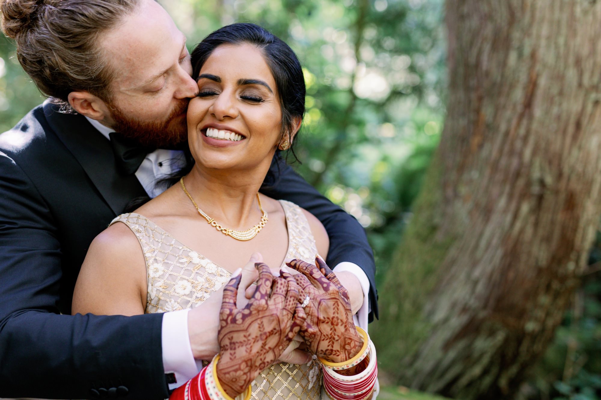 Groom kissing the bride on the cheek, bride smiling with closed eyes.