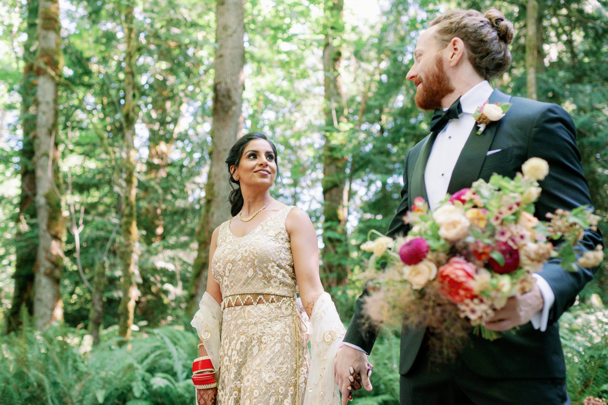 Couple holding hands and looking at each other lovingly in the forest.