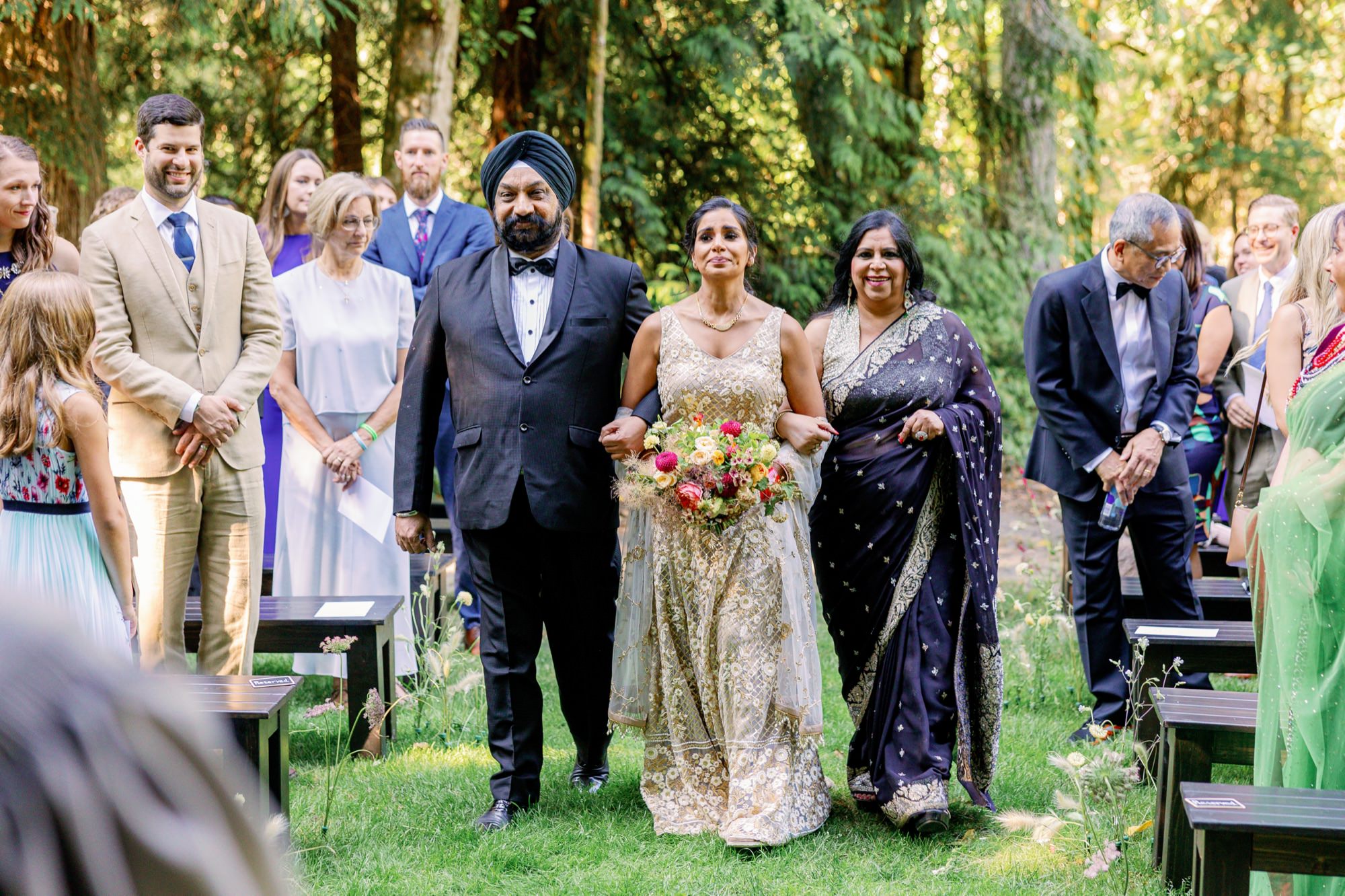 Bride walking down the aisle with her parents during an outdoor wedding ceremony.