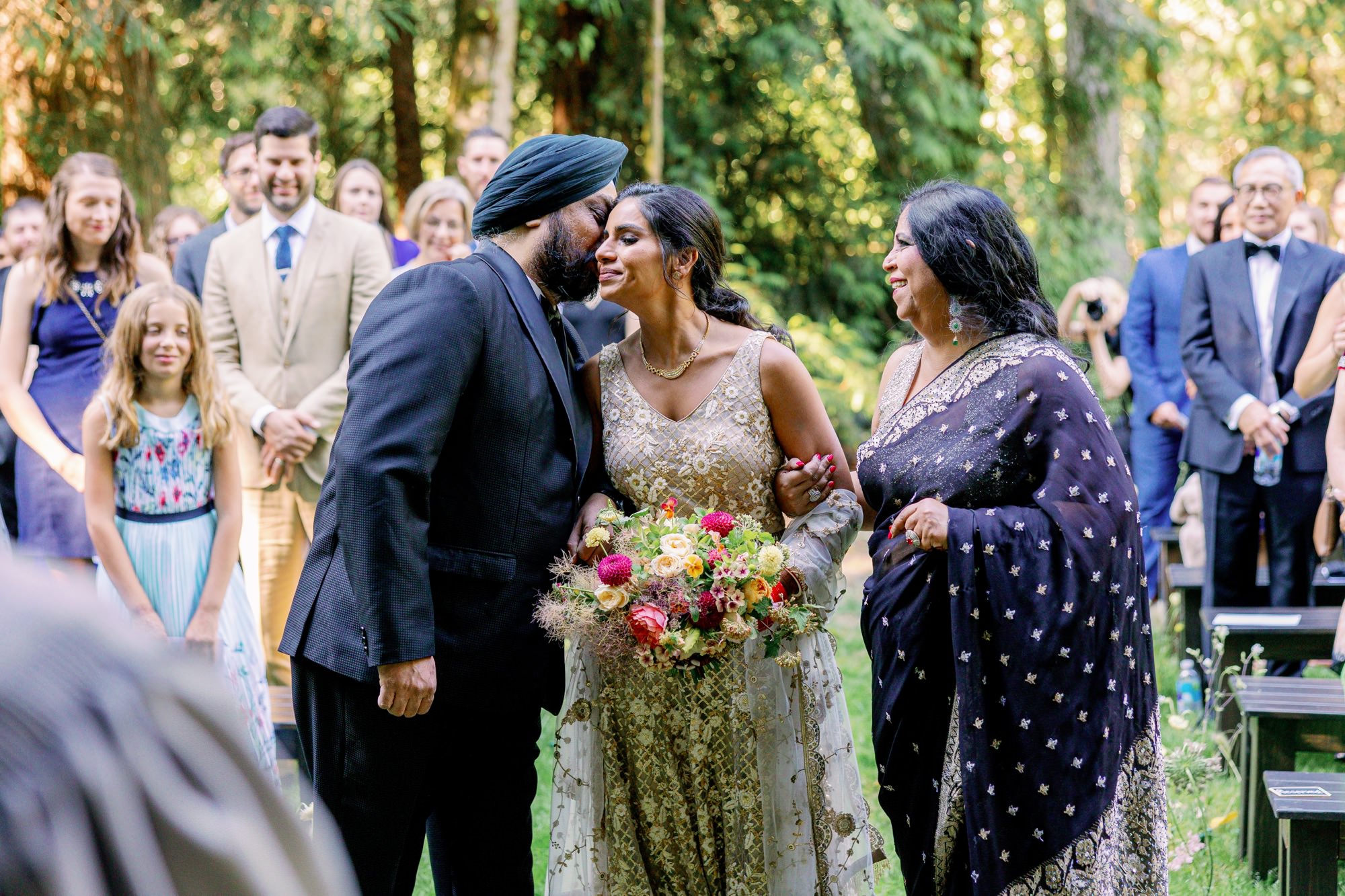 Bride receiving a kiss from her father while holding her mother’s hand during the wedding ceremony.