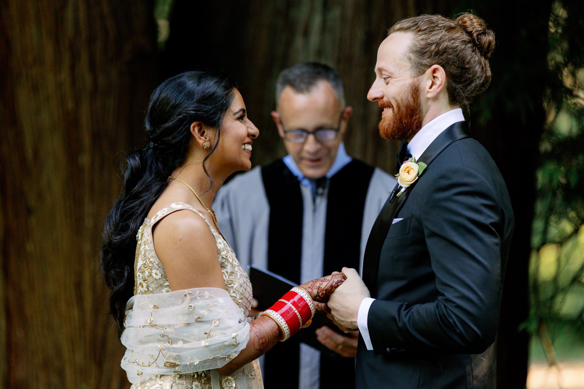 Bride and groom smiling at each other while holding hands during the ceremony.