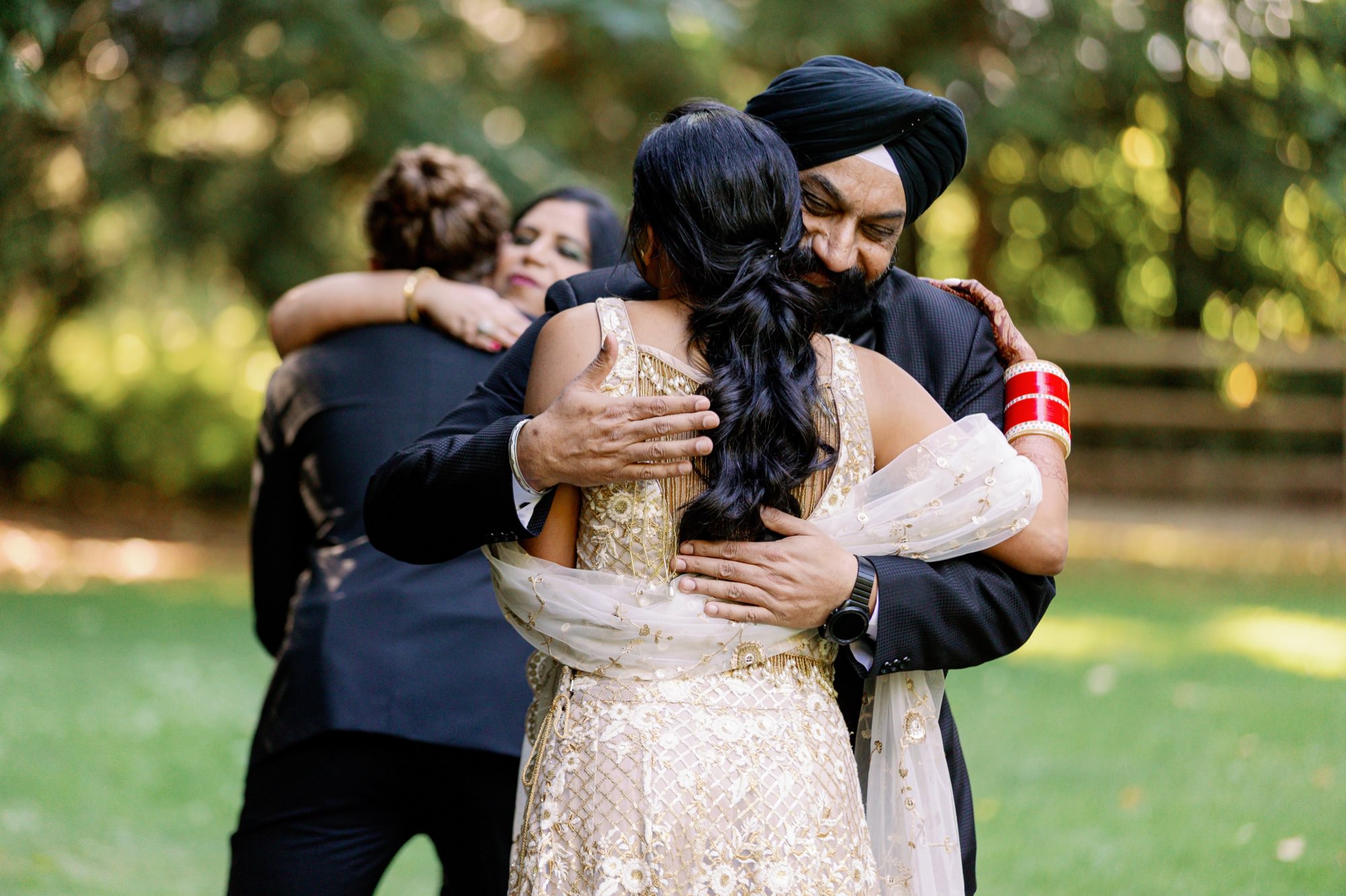 Emotional embrace between bride and her father; groom hugging a family member.