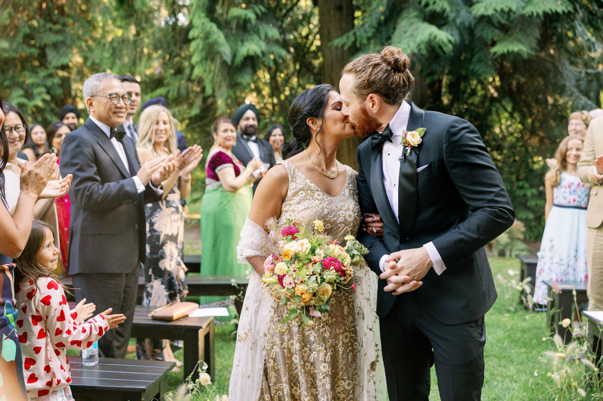 Bride and groom sharing a celebratory kiss surrounded by guests.