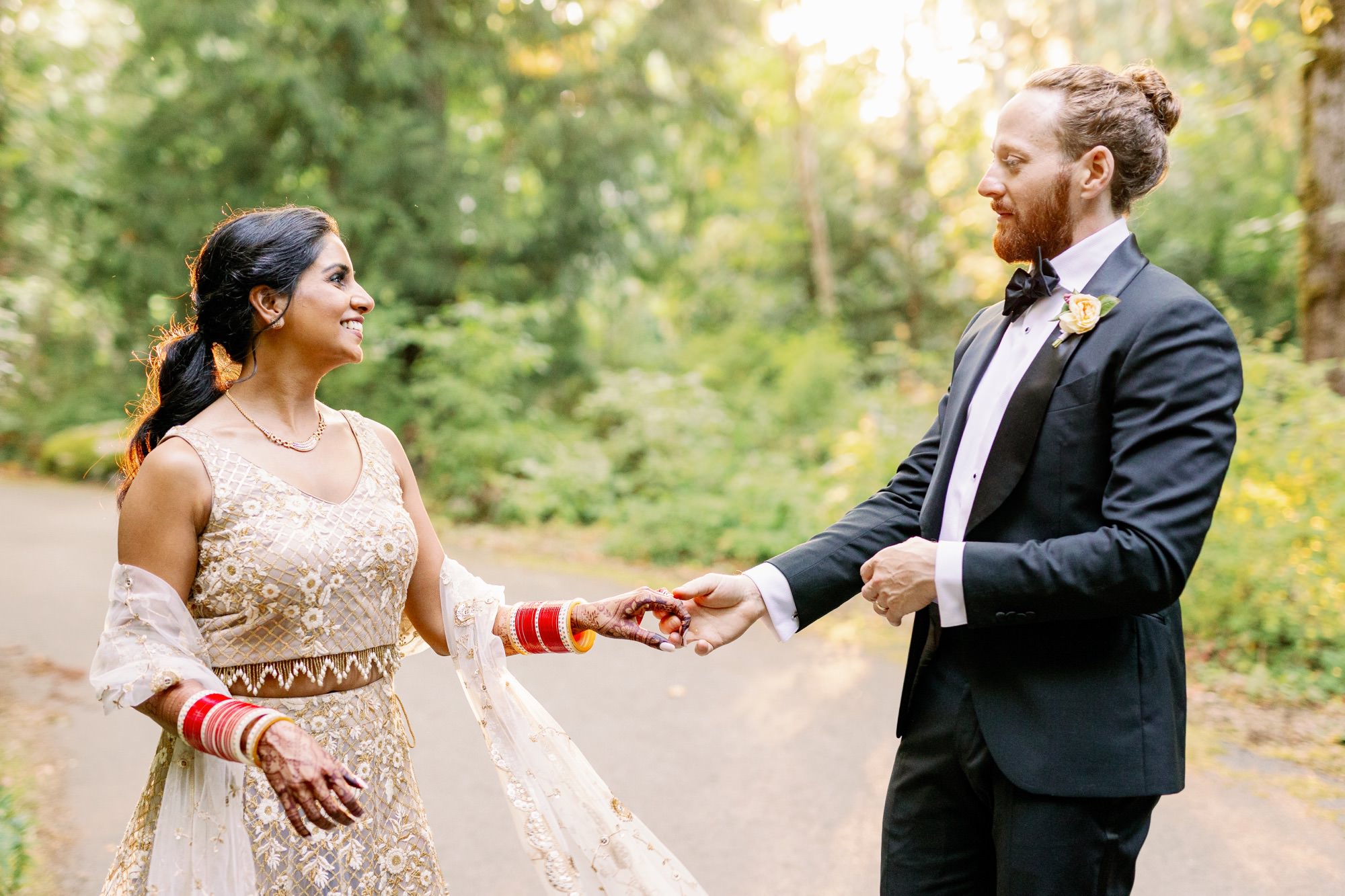 Bride and groom dancing on a wooded path, bathed in sunlight.