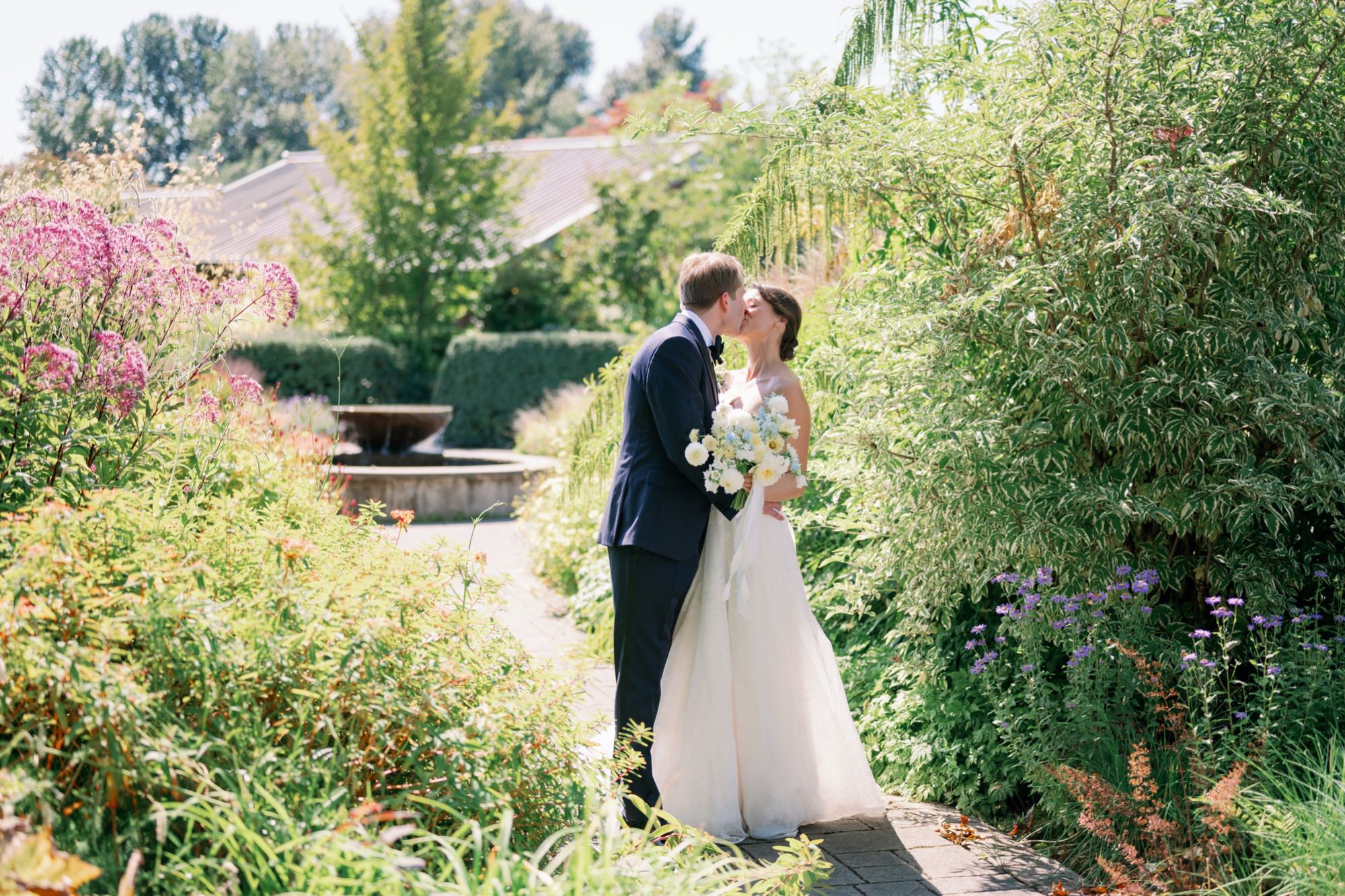 Wedding couple posing for portraits along the natural garden paths at the Center for Urban Horticulture, framed by green foliage.