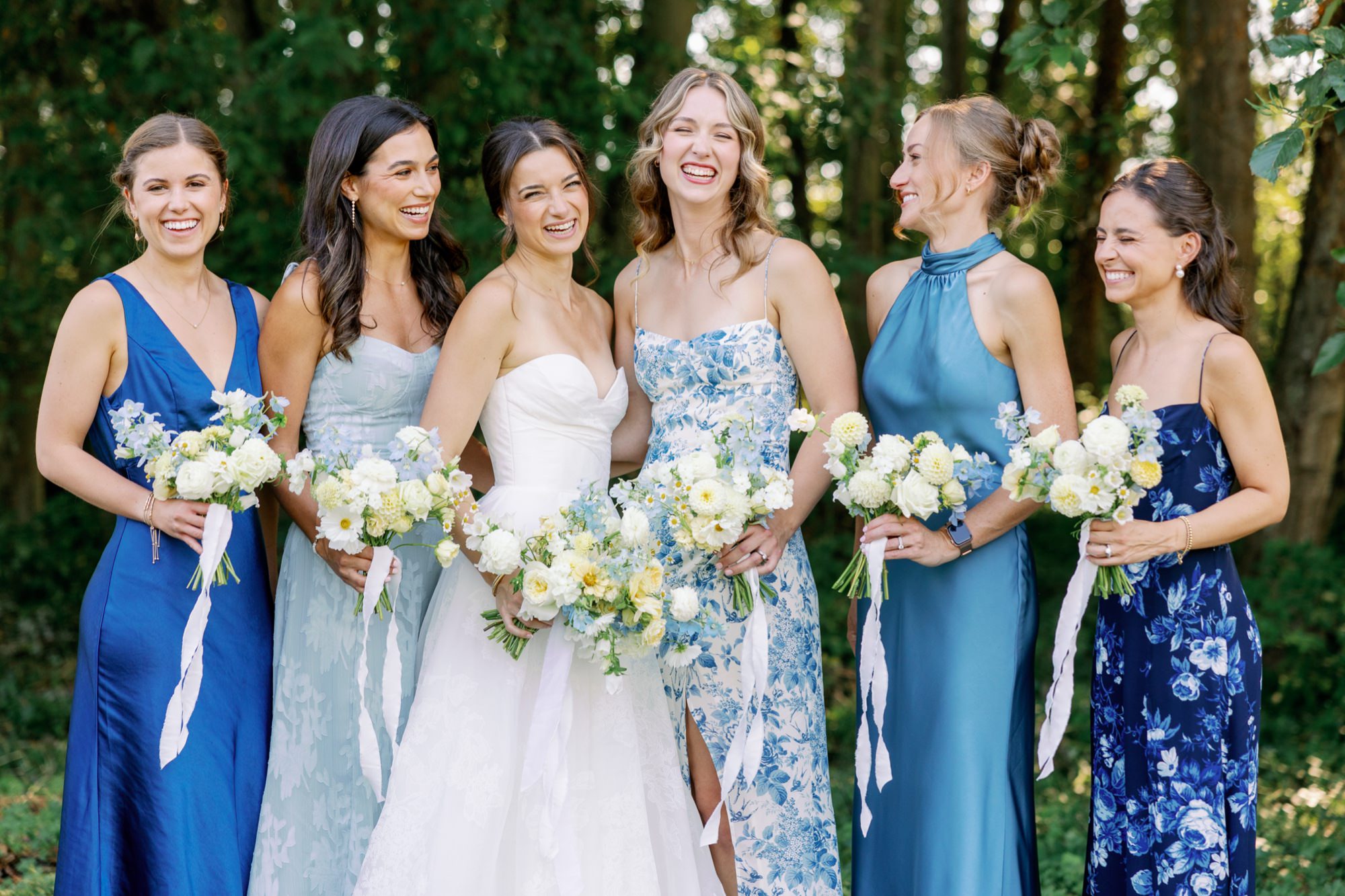 Bridesmaids laugh together with greenery in the background.