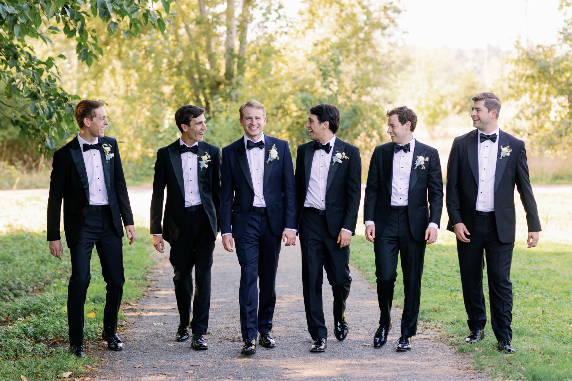 Groomsmen walk with the groom along a path in a field at the Center for Urban Horticulture.