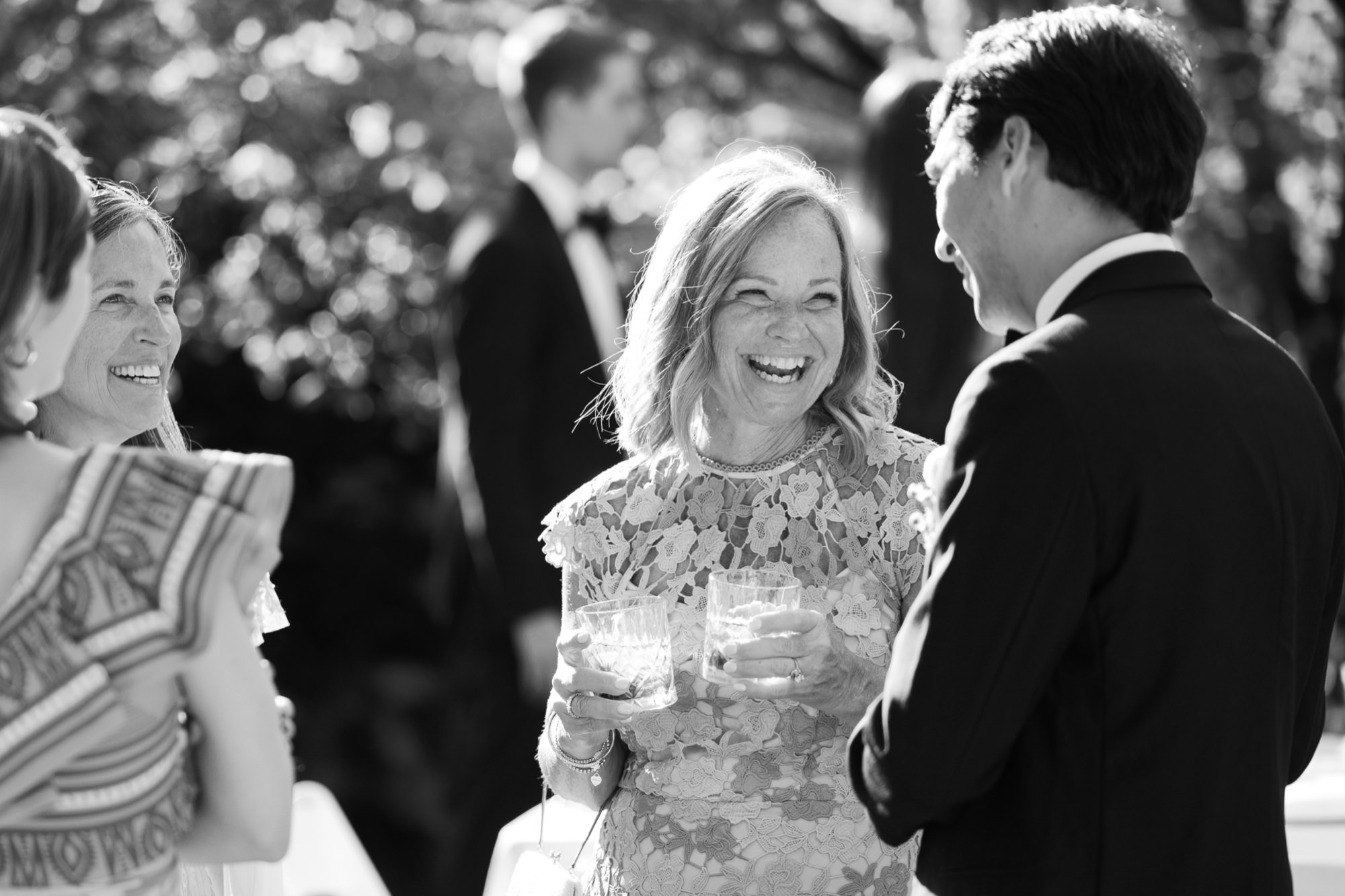 Guests mingle in the orchard during cocktail hour, smiling, hugging, and holding drinks as they celebrate.