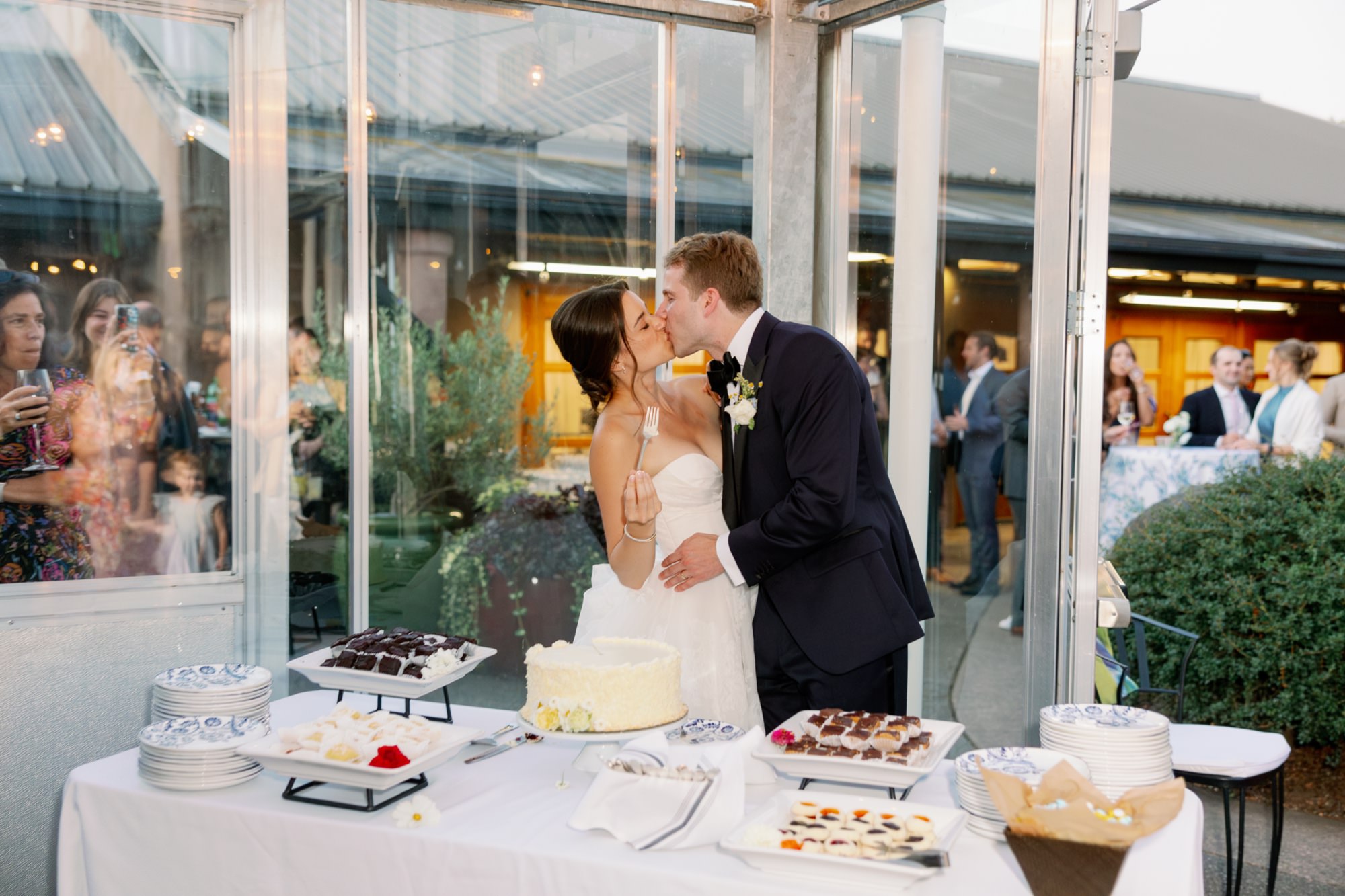 The wedding couple shares a kiss after cutting their cake in the atrium at the Center for Urban Horticulture.