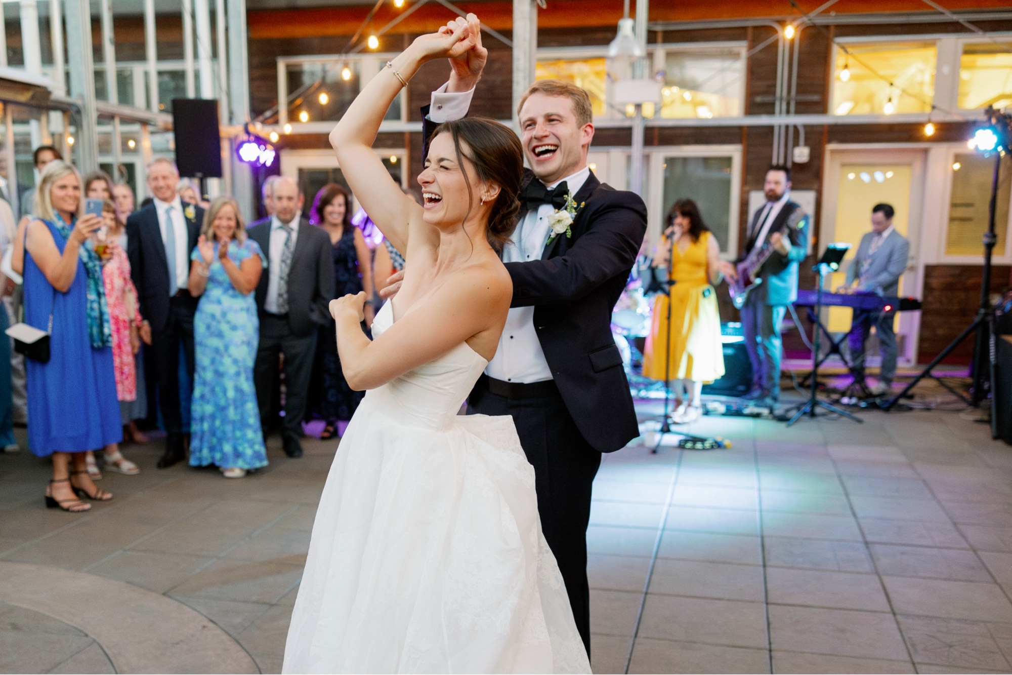 The groom spins the bride during their first dance in the atrium at the Center for Urban Horticulture while the band plays in the background.