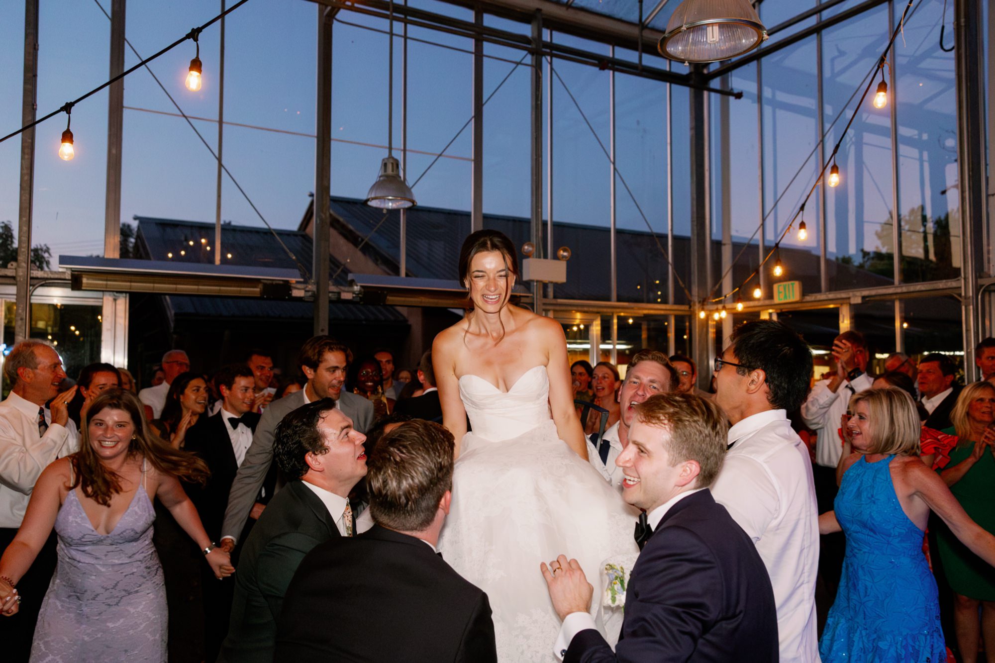 Bride gets lifted into the air during the Hora in the atrium at Center for Urban Horticulture.