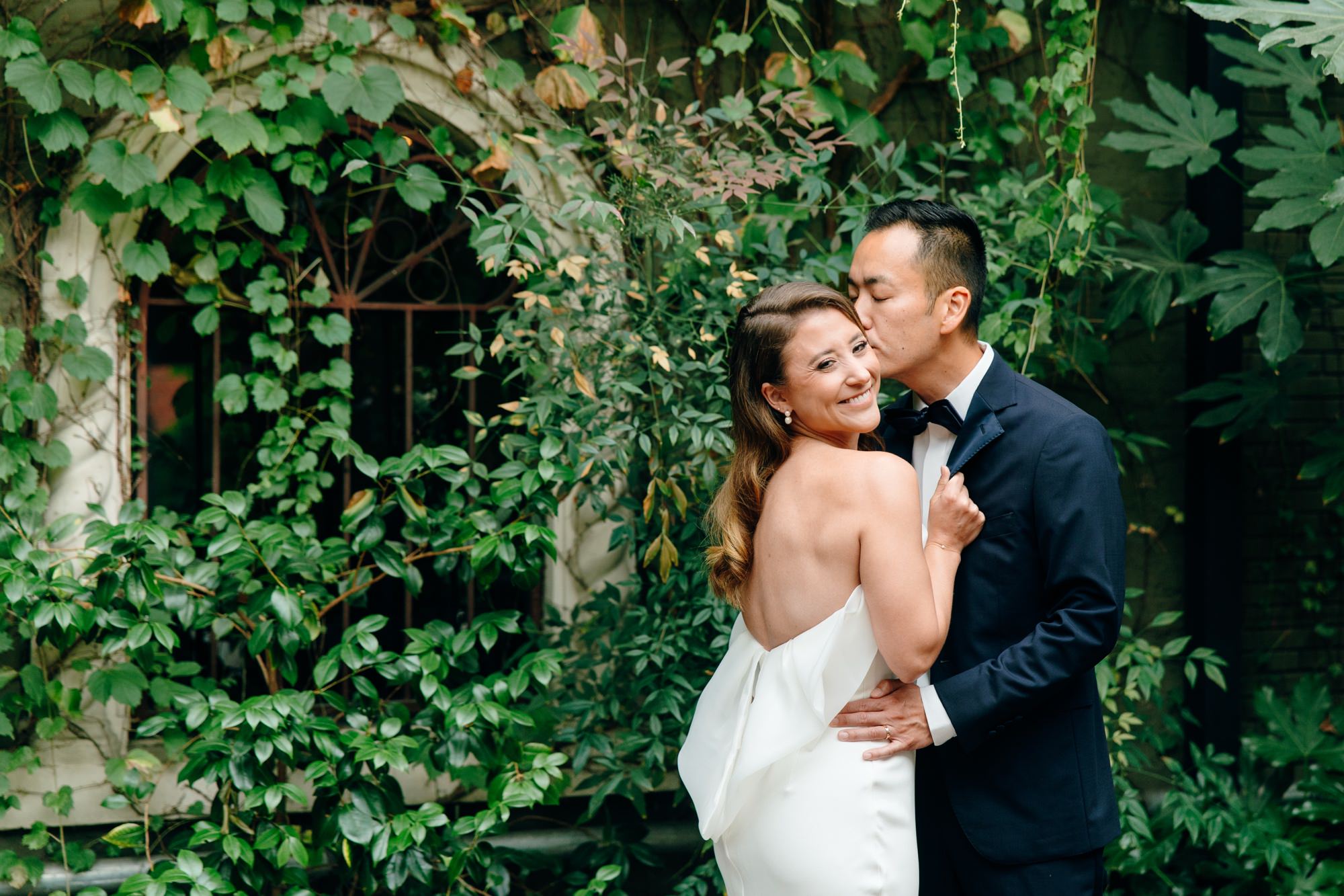 Groom kisses bride on her head while posing for wedding portraits.