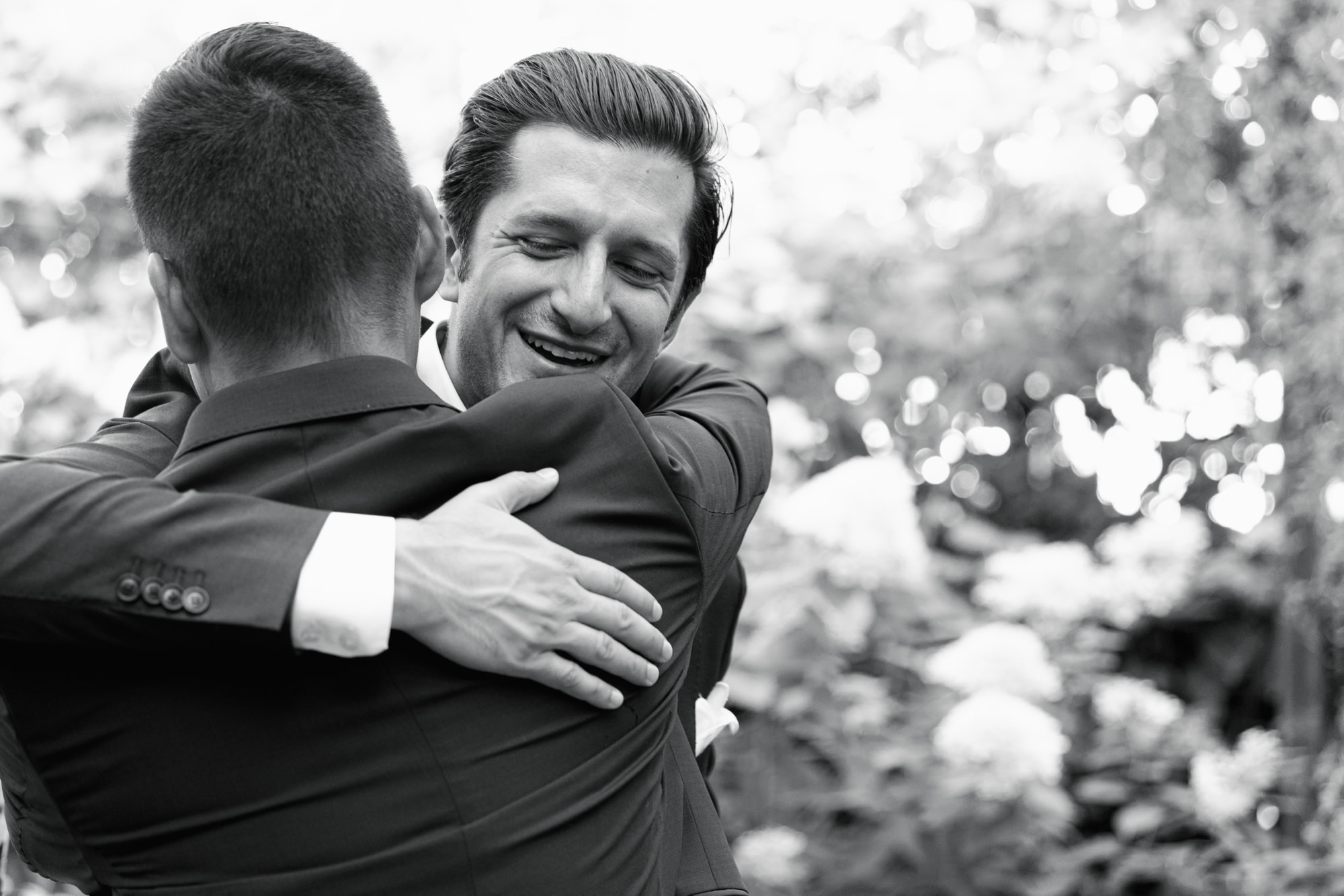 A wedding guest hugs the groom and smiles during cocktail hour