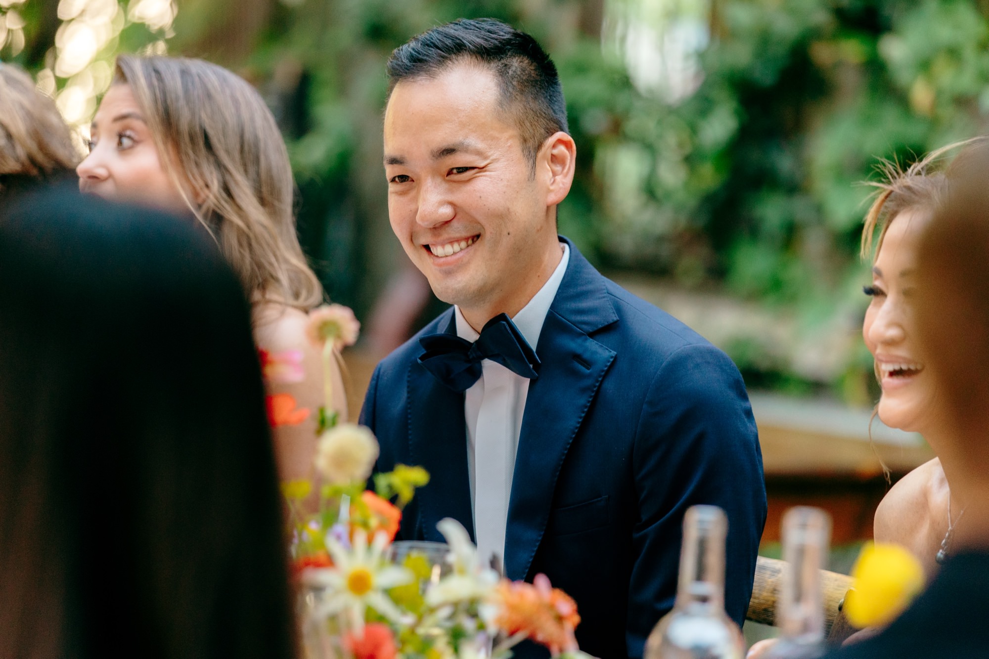 The groom smiles while sitting at the dinner table with guests.