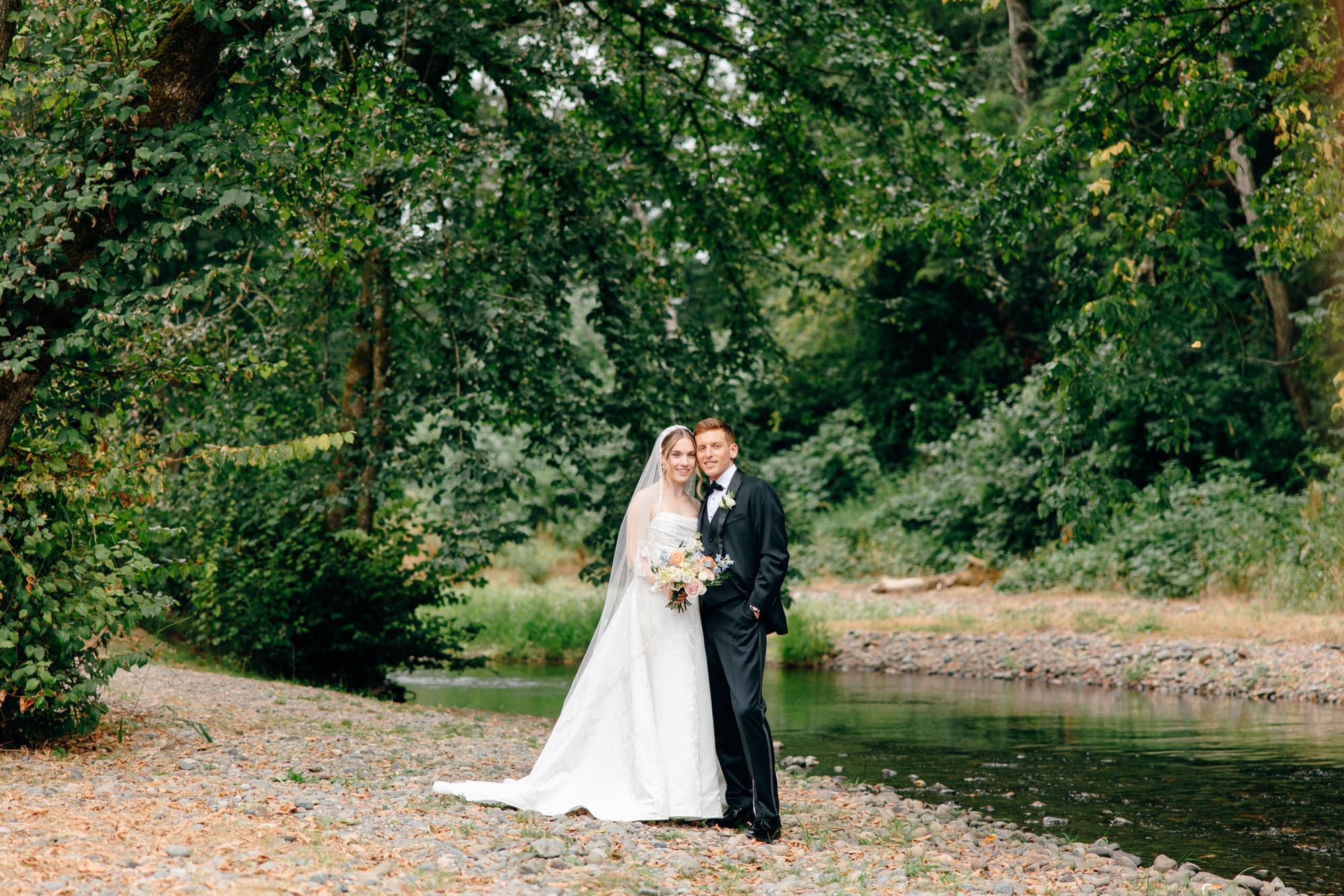 Wedding couple posing in front of the creek at Fox Hollow Farm, surrounded by lush greenery, capturing a romantic outdoor Seattle wedding moment.