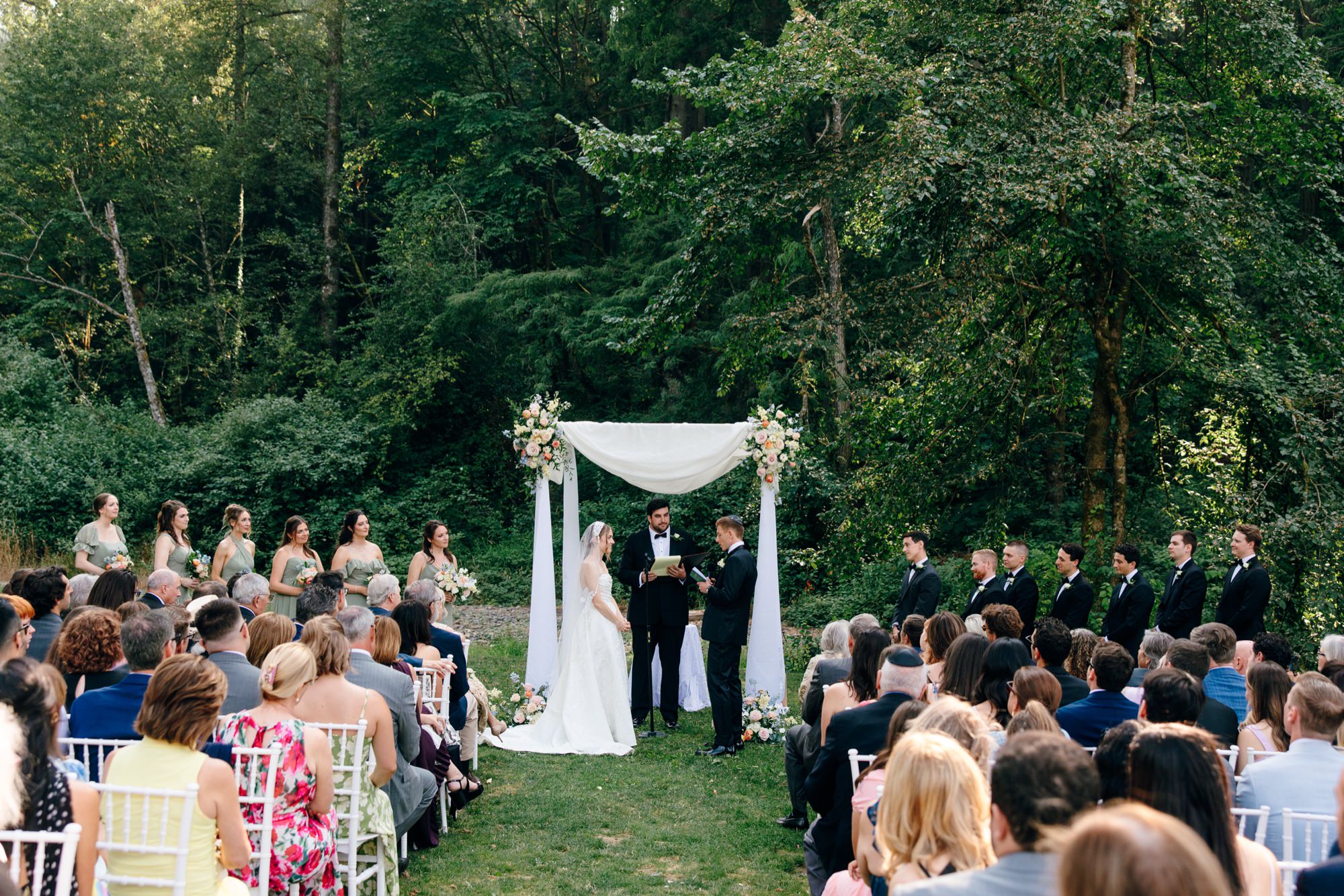 Wedding couple exchanging vows by the creek at Fox Hollow Farm, surrounded by lush greenery, capturing a romantic outdoor Seattle wedding moment.